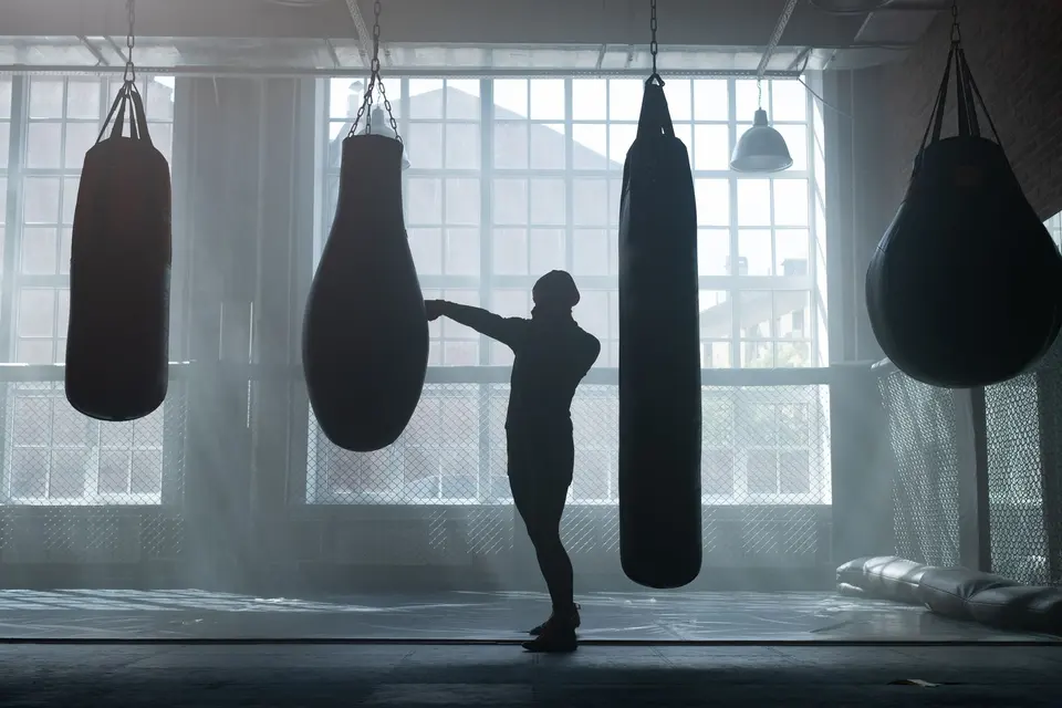 Silhueta de uma pessoa treinando no saco de pancada em uma academia de boxe